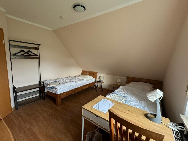 Doppelzimmer im Haus Willbrok mit zwei Betten, Schreibtisch und Kleiderständer.