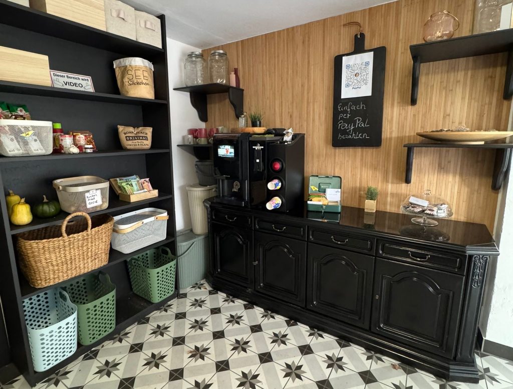 Innenansicht des Hofladens Tante Willbrok mit Regalen voller Produkte, einer Kaffeemaschine und einer PayPal-Zahlungsoption.