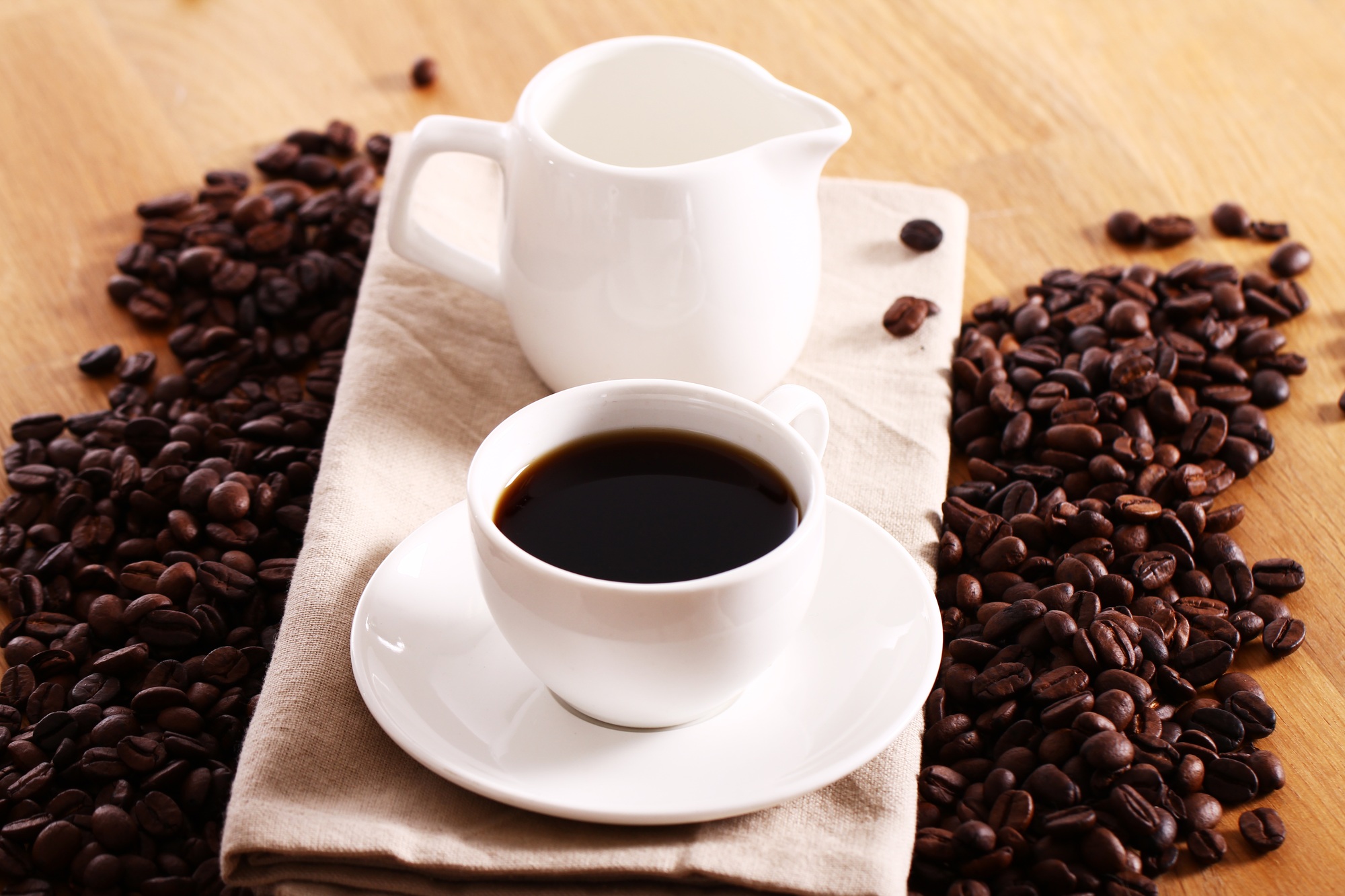 Eine Tasse frisch gebrühter Kaffee und eine Kaffeekanne auf einem Tisch, umgeben von Kaffeebohnen.