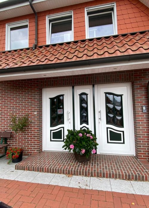 Eingang von Haus Willbrok mit zwei Türen, einer Bank und Blumen auf der Veranda.